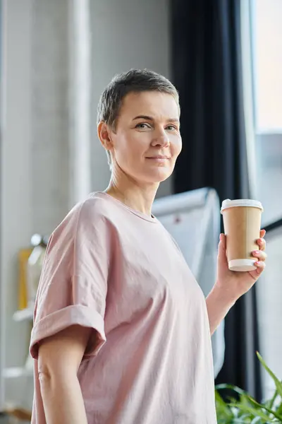 Una mujer con una camisa rosa saborea una taza de café. - foto de stock