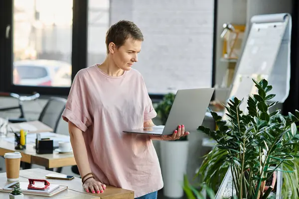 Attractive woman, in a bright pink shirt, works diligently on a laptop. — Stock Photo