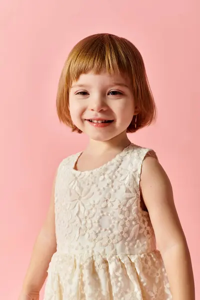 Маленька дівчинка в білій сукні позує за портрет на рожевому тлі. — стокове фото