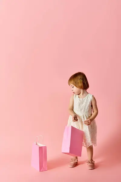 Adorable fille en robe blanche tenant des sacs à provisions sur fond rose. — Photo de stock