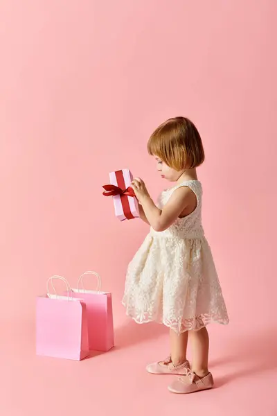 Little girl in white dress joyfully holds a pink gift box. — Stock Photo