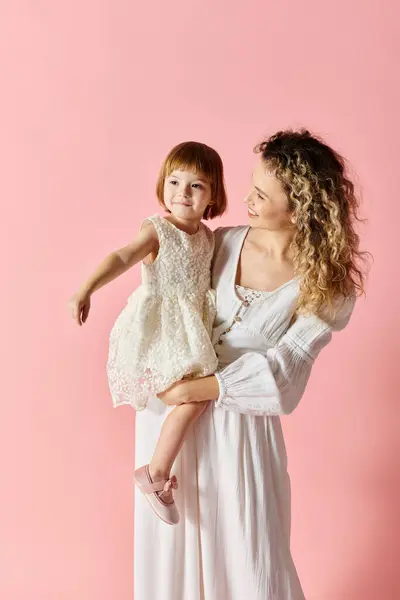 Una madre encantadora en blanco con el pelo rizado sostiene a un bebé en un vestido blanco. - foto de stock