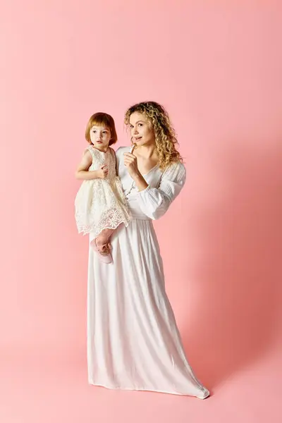 A woman in white dress holds a baby girl in a white dress against a pink background. — Stock Photo