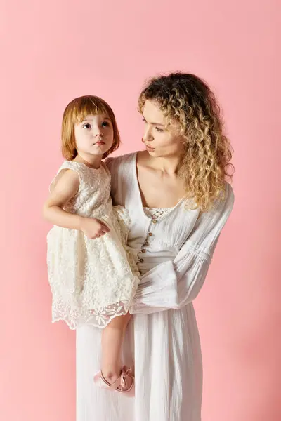 A mother holding her little girl in a white dress on a pink background. — Stock Photo