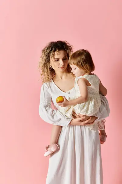 Woman holding child in white dress on pink background. — Stock Photo