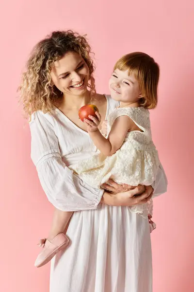 Madre e figlia che tengono una mela su uno sfondo rosa. — Foto stock