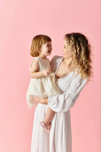 Eine Frau hält ihre kleine Tochter auf einem zartrosa Hintergrund. — Stockfoto