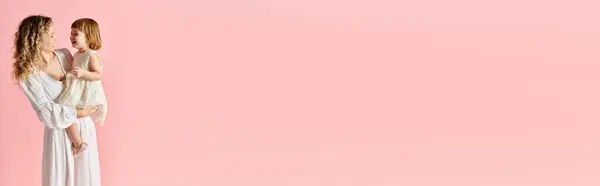 A woman in a pink background cradling her baby girl in her arms. — Stock Photo