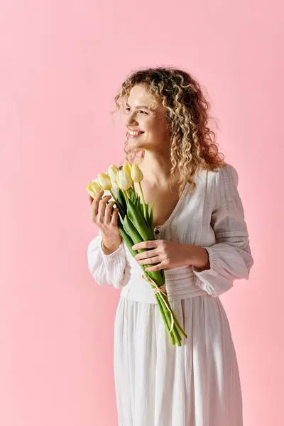 Женщина в белом платье держит тюльпаны на розовом фоне. — стоковое фото