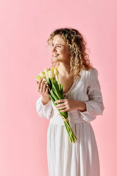 Woman in white dress holds tulips on pink background. — Stock Photo