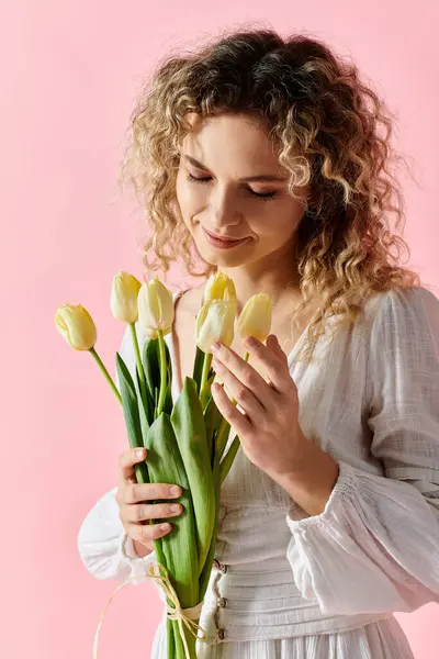 Жінка тримає жовтий букет тюльпанів на рожевому тлі. — стокове фото