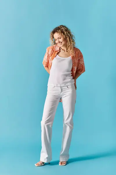 Stylish woman with curly hair strikes a pose in white pants against a vibrant blue backdrop. — Stock Photo