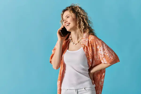 Woman with curly hair talking on cell phone against vibrant blue background. — Stock Photo