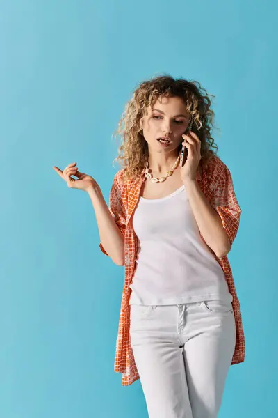 Curly-haired woman talking on cell phone against blue backdrop. — Stock Photo