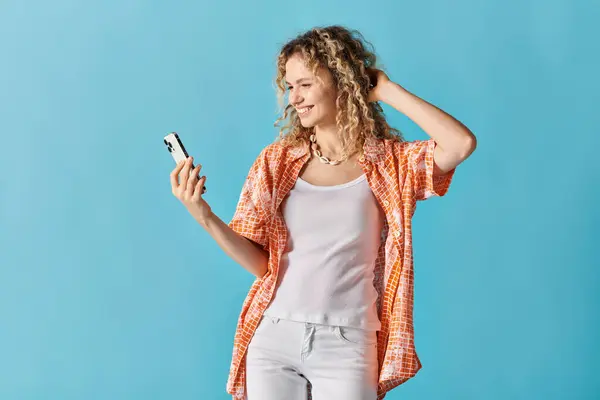 Eine junge Frau mit lockigem Haar mit einem Handy vor blauem Hintergrund. — Stockfoto
