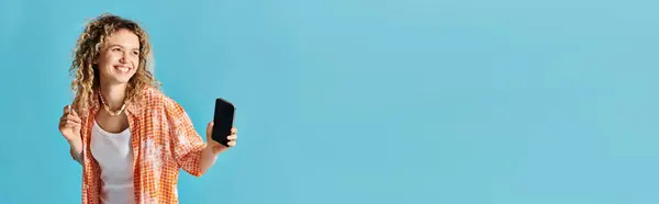 Frau mit lockigem Haar hält Handy vor leuchtend blauem Hintergrund. — Stockfoto