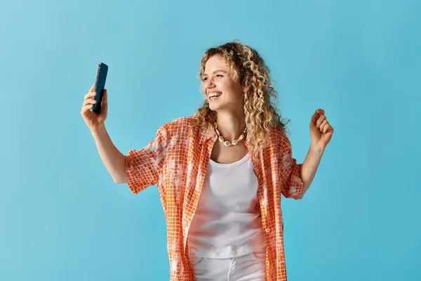 Stylish woman with curly hair holding phone against a vibrant blue background. — Stock Photo