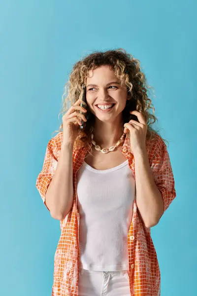 Young woman with curly hair talking on phone against blue backdrop. — Stock Photo