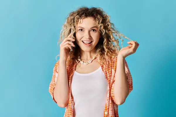Eine junge Frau mit lockigem Haar spricht auf ihrem Handy vor einem leuchtend blauen Hintergrund. — Stockfoto