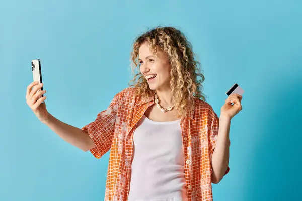 A woman with curly hair snaps a selfie holding a credit card. — Stock Photo