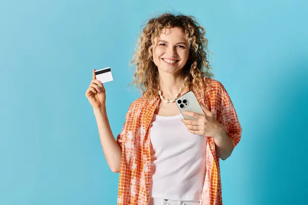 Young woman with curly hair holding credit card and cell phone against colorful backdrop. — Stock Photo