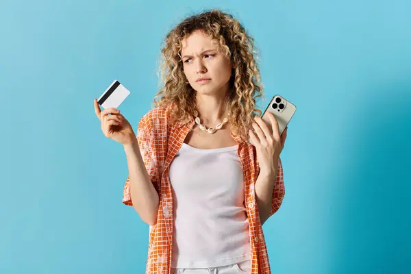 A woman with curly hair holding credit card and a cell phone. — Stock Photo