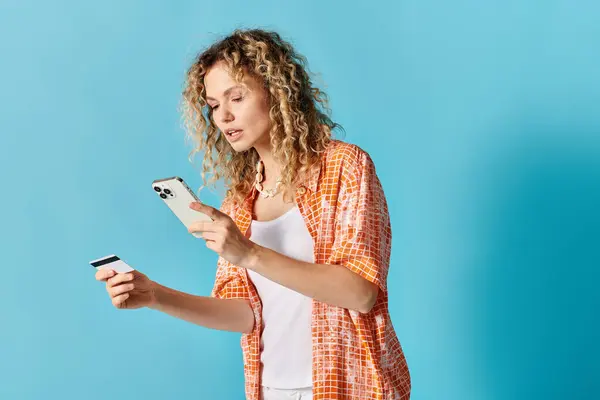 Mulher com cabelo encaracolado detém telefone celular e cartão de crédito. — Fotografia de Stock
