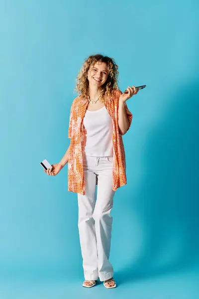 Donna dai capelli ricci che tiene il telefono cellulare sullo sfondo blu. — Foto stock