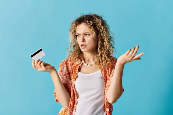 A stylish woman with curly hair holding a credit card against a vibrant backdrop. — Stock Photo