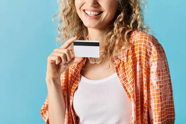 Woman with curly hair holding credit card on blue backdrop. — Stock Photo