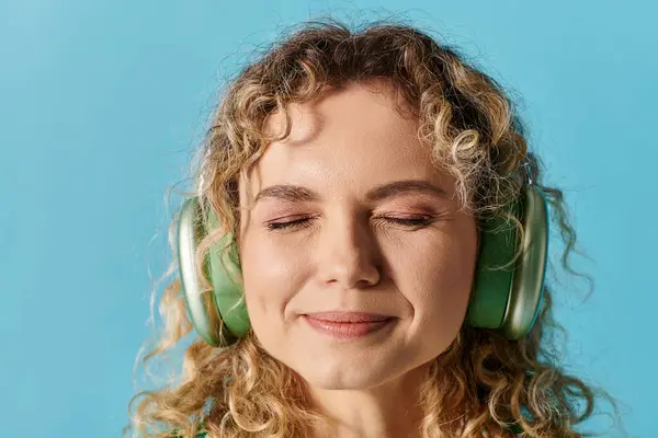 Lockenmähnige Frau mit grünen Kopfhörern vor lebendiger Kulisse. — Stockfoto