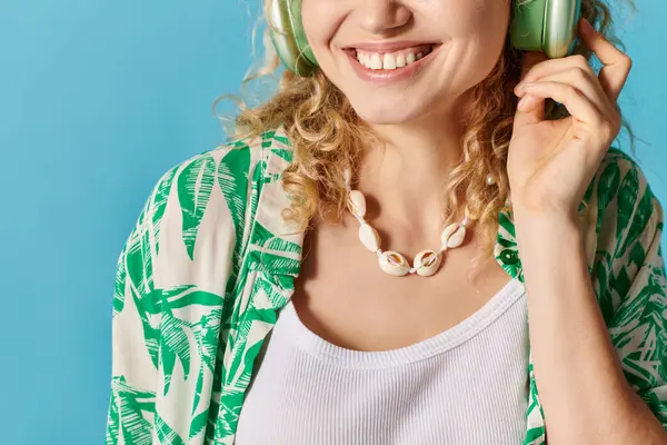 Femme rayonnante aux cheveux bouclés sourit et écoute de la musique sur un fond bleu. — Photo de stock