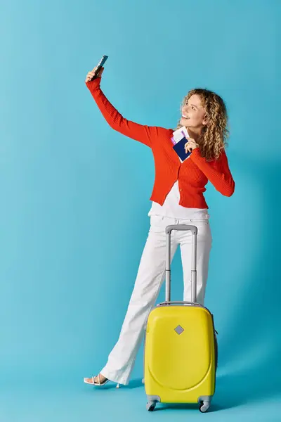 Curly-haired woman taking selfies with a yellow suitcase. — Stock Photo
