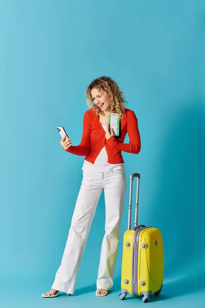 Femme aux cheveux bouclés tenant une valise jaune, vérifiant le téléphone. — Photo de stock