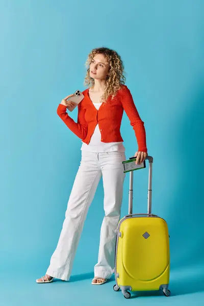 A woman with a yellow suitcase strikes a pose against a vibrant blue background. — Stock Photo