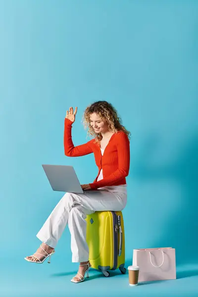 Кучерява жінка сидить на валізі, загорнута в ноутбук. — стокове фото