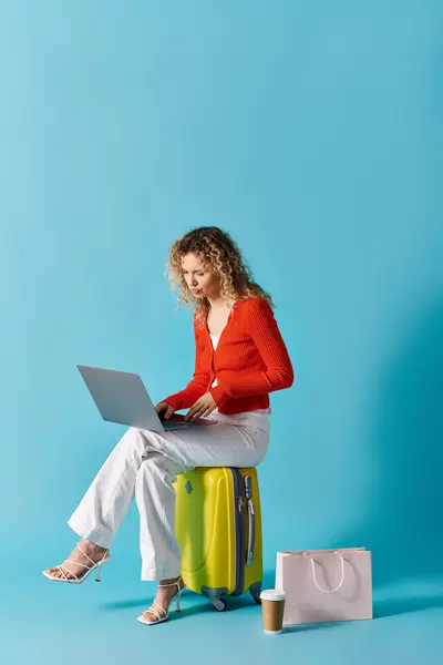 Woman sitting on a suitcase, using a laptop. — Stock Photo