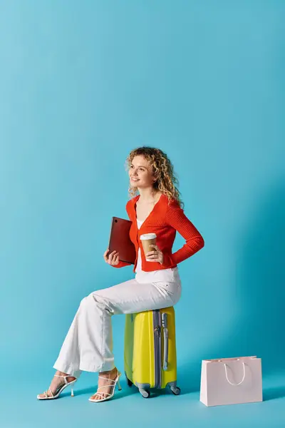 A woman with curly hair sits on a suitcase, enjoying a cup of coffee. — Stock Photo