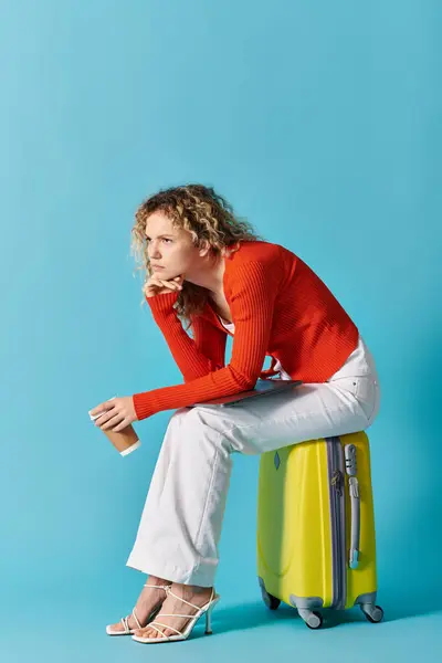 A stunning woman with curly hair sits atop a bright yellow suitcase. — Stock Photo