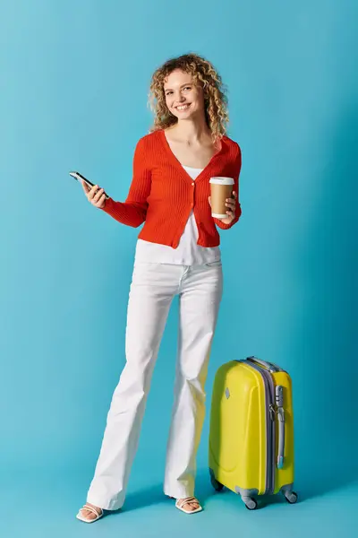 A stylish woman holding a cup of coffee and a suitcase on a blue background. — Stock Photo