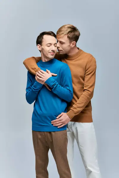 Loving gay couple in casual attire standing side by side on a gray backdrop. — Stock Photo