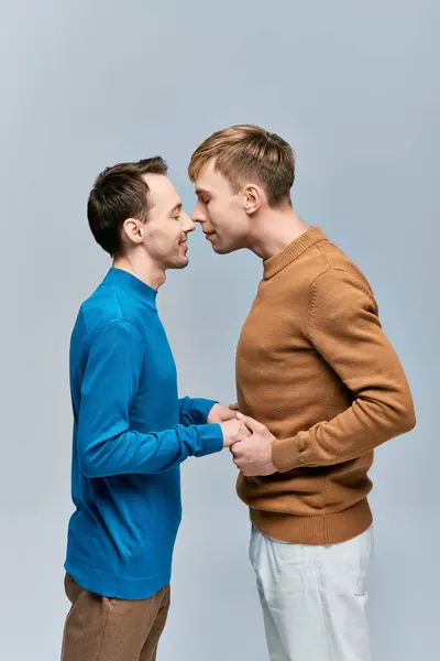 Two young men, a loving gay couple, stand together in casual attire against a gray backdrop. — Stock Photo
