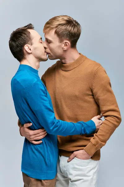 Loving gay couple in casual attire standing alongside each other on a gray backdrop. — Stock Photo