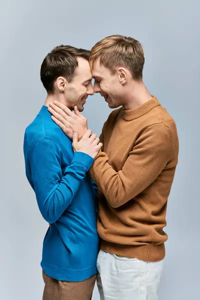 Deux hommes en tenue décontractée s'embrassent, debout côte à côte sur un fond gris. — Photo de stock