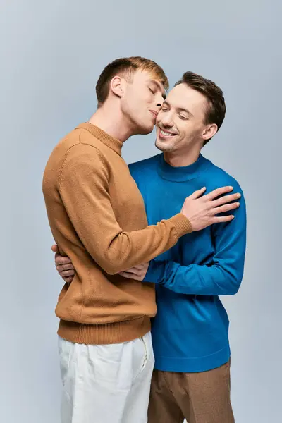 Zwei Männer in Freizeitkleidung stehen nebeneinander, die Arme umeinander vor grauem Hintergrund. — Stockfoto