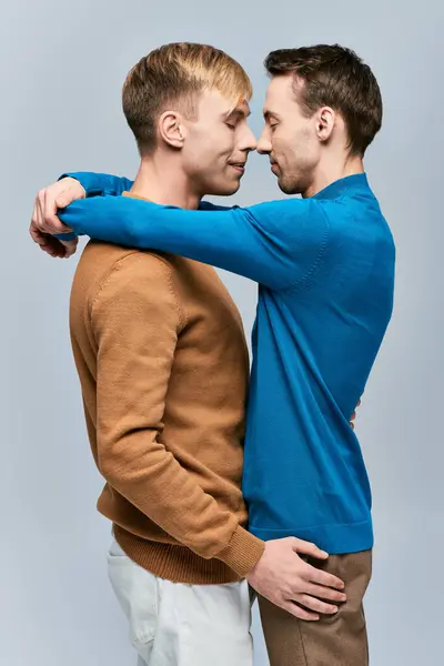 Dos hombres en atuendo casual de pie uno al lado del otro con los brazos alrededor del otro en un fondo gris. - foto de stock