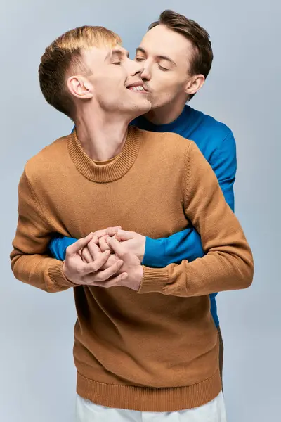 Двоє чоловіків в светрах ласкаво цілуються на сірому тлі. — стокове фото