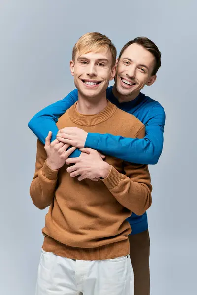 Двоє молодих чоловіків в повсякденному вбранні обіймаються ласкаво на сірому тлі. — стокове фото