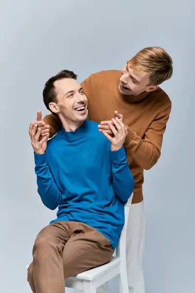 Dois homens de traje casual sentados em uma cadeira branca, compartilhando risos e um momento especial. — Fotografia de Stock