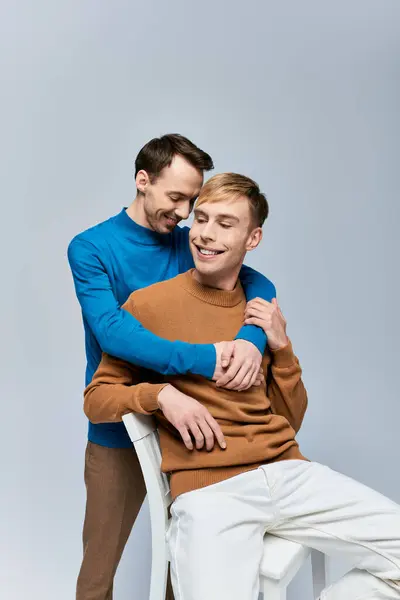 Two men sit on a chair, arms around each other, showcasing love and connection. — Stock Photo